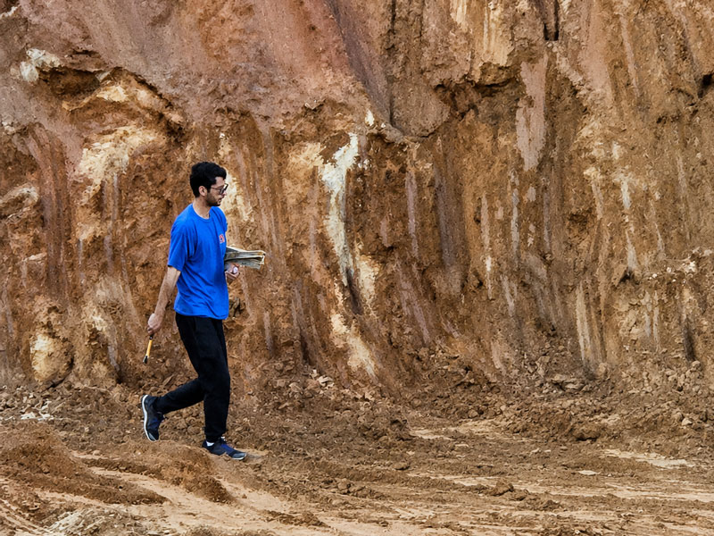 Técnico da IMS atravessando um corte de terreno com as plantas do projeto em mãos