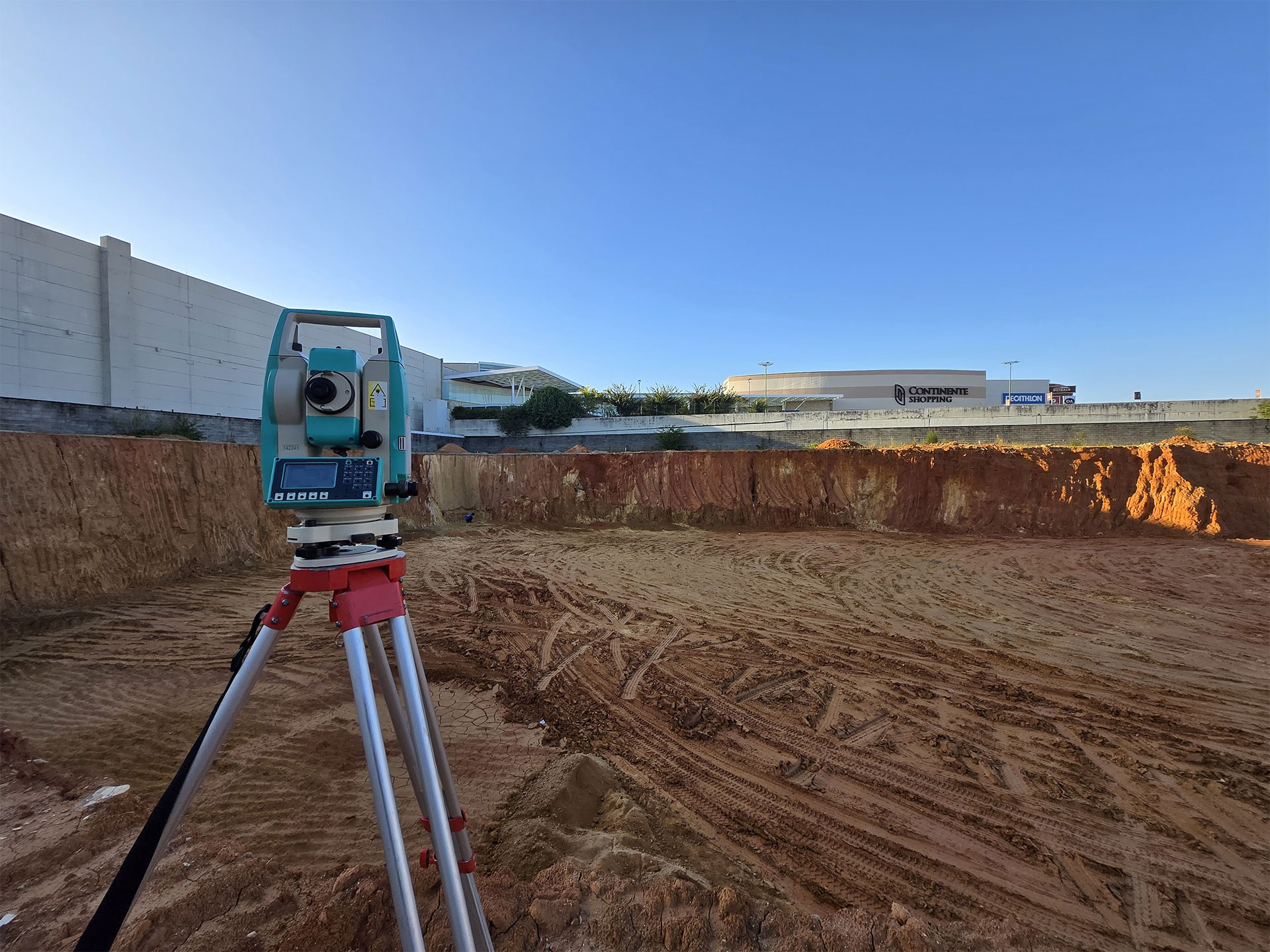 Estação total montada em tripé durante levantamento topográfico em terreno terraplenado